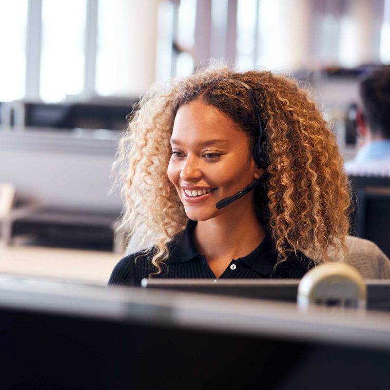 Young girl wearing a headset smiling and talking to a customer.